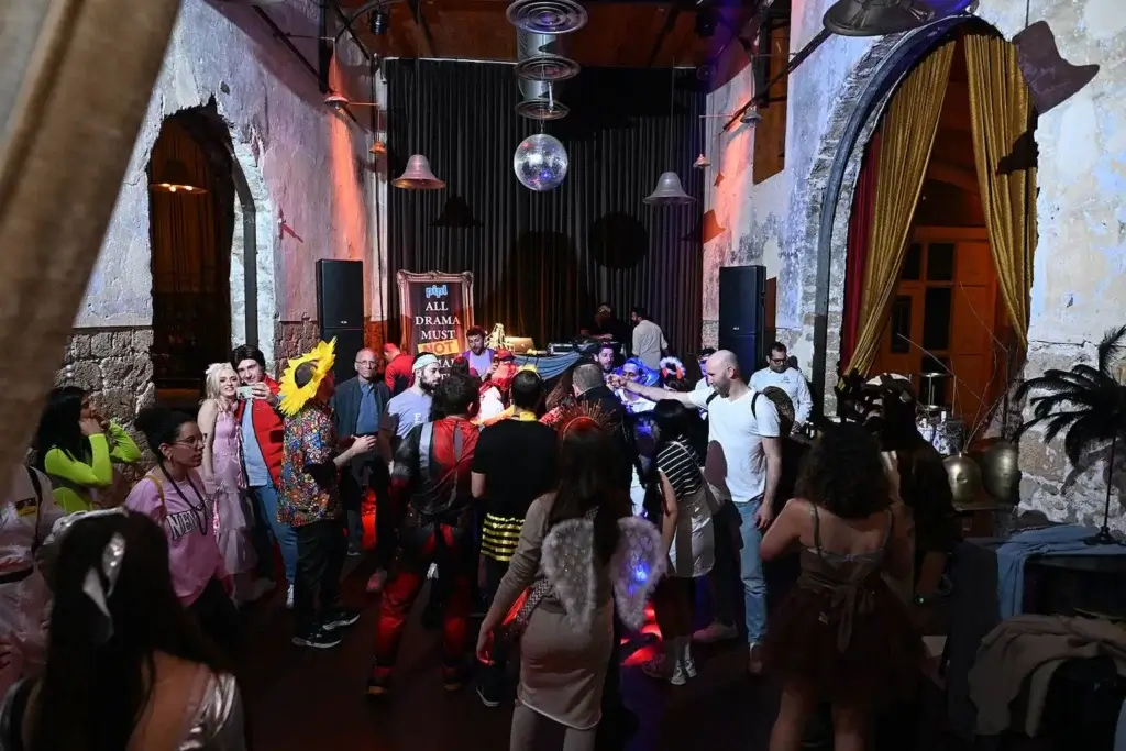 אנשים חוגגים במסיבת פורים לעובדים של חברה, באולם אירועים מעוצב עם תאורה צבעונית